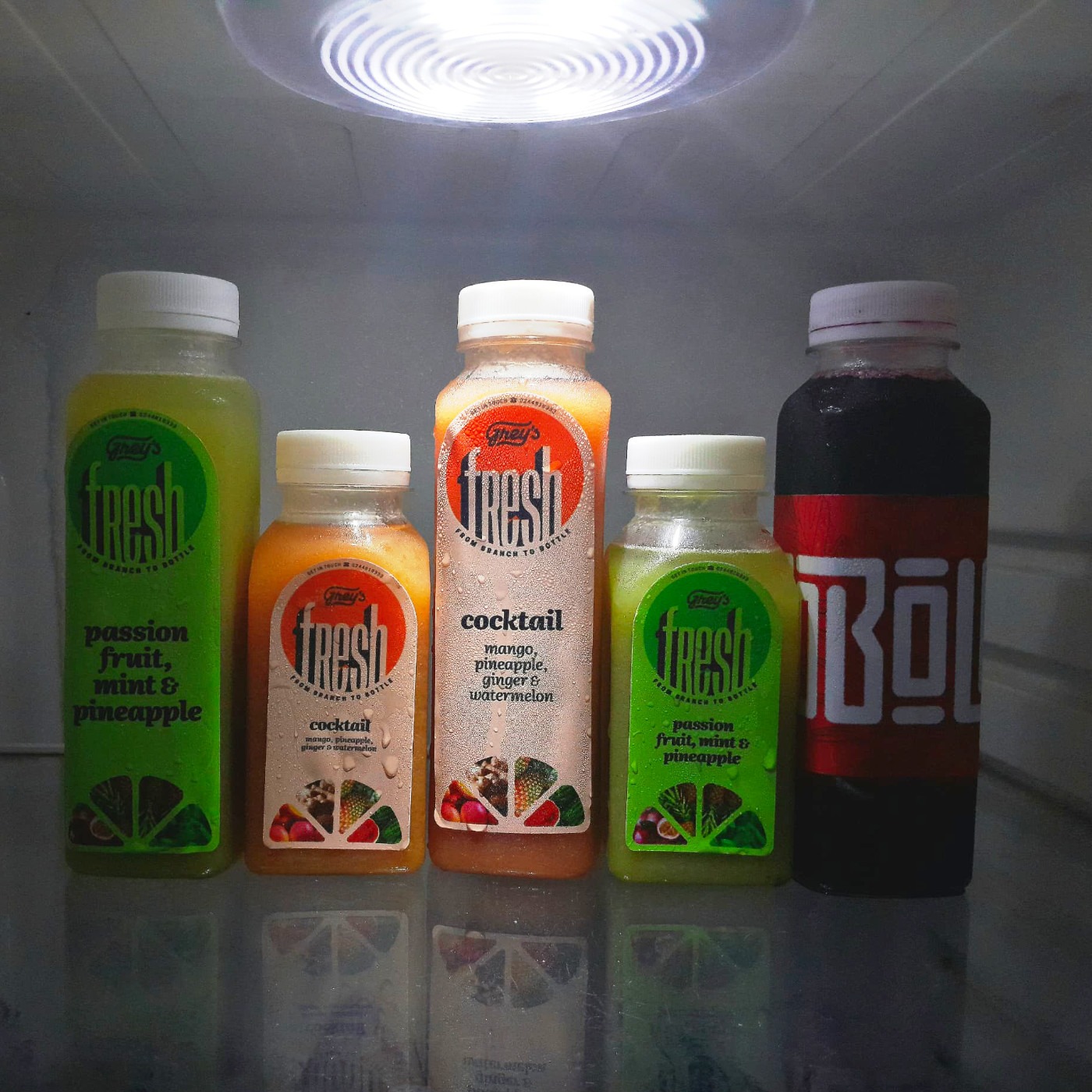 Five colourful juice and sobolo bottles under a harsh refrigerator light